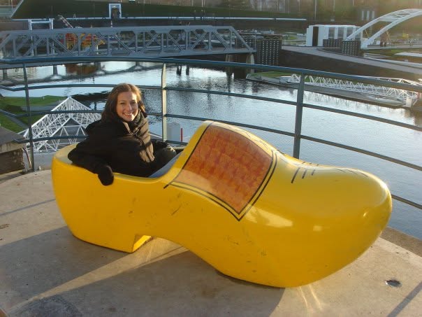 A person sitting in a large yellow wooden shoe sculpture overlooking a river.